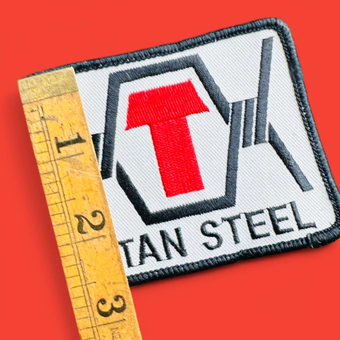 Vintage 1990's Titan Steel Embroidered Patch featuring a red 'T' on a white background, measuring 2.5" x 3.5".