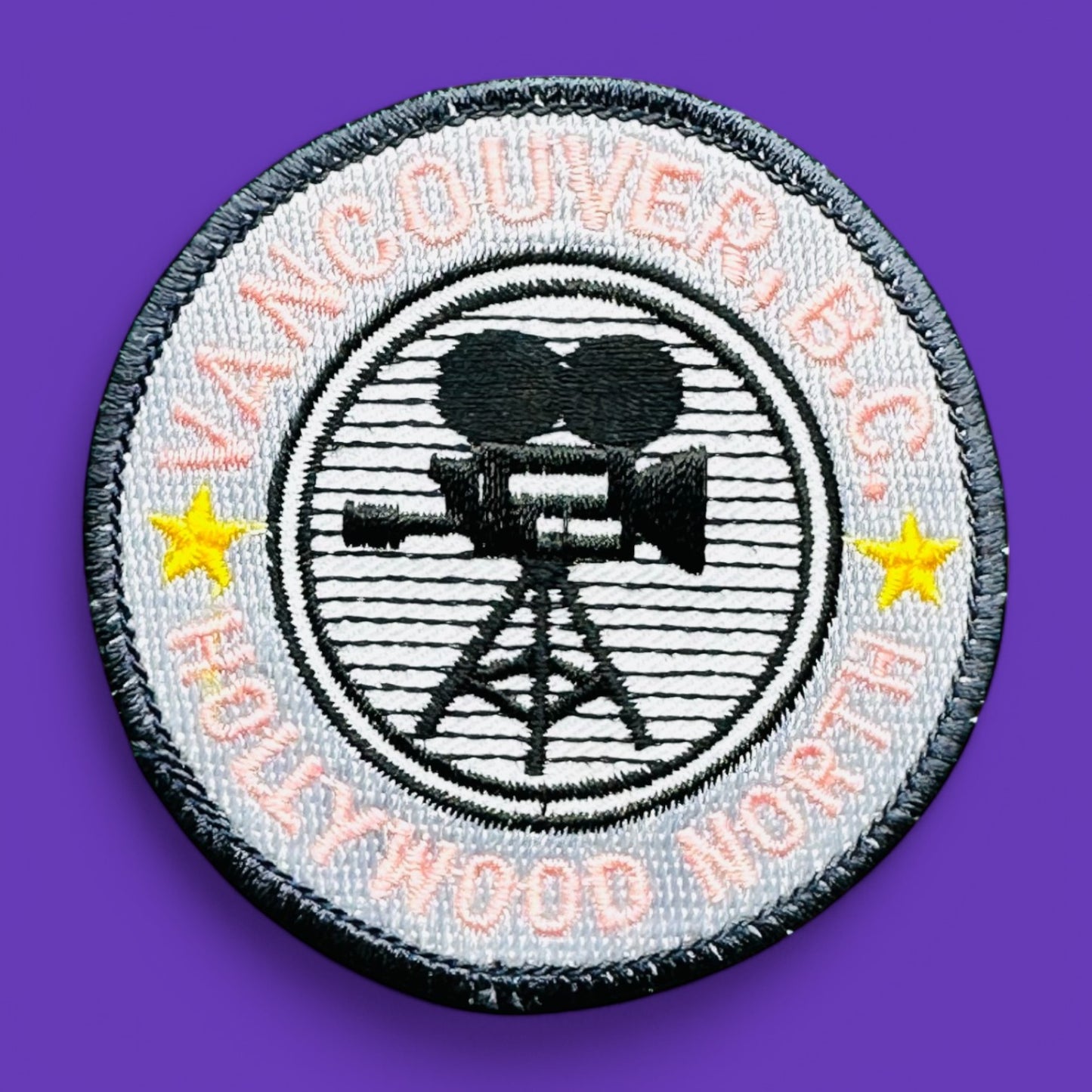 Vancouver BC, Hollywood North Embroidered Patch, 1980's features pink lettering and a film camera design on a grey background.