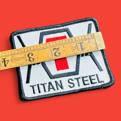 Vintage 1990's Titan Steel Embroidered Patch featuring black text, red capital T, and black edging on a white background.