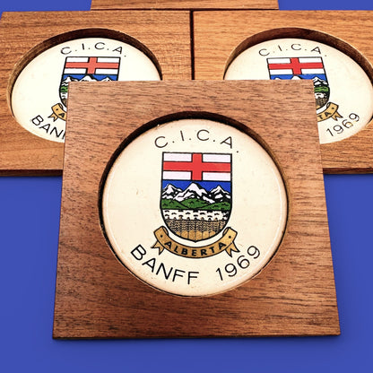 MCM 1960's Teak Drink Coaster Set | Convention: C.I.C.A Banff Alberta 1969 features a stylish Alberta crest and mountains.