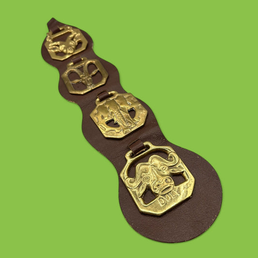 Brass horse adornments on a brown leather strap featuring African animals like buffalo and elephant. Horse, brass, African animals.